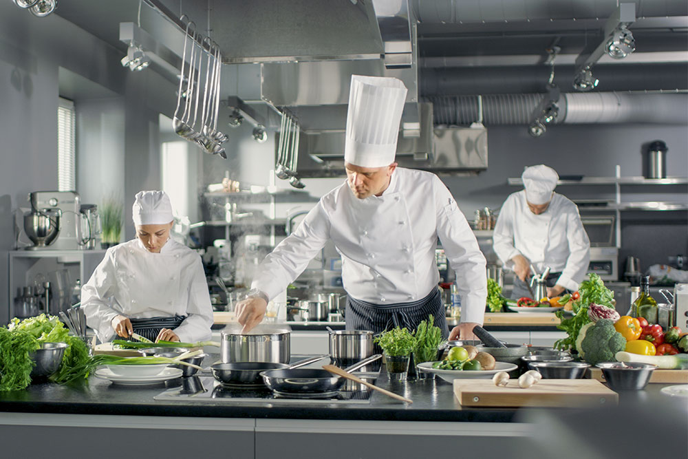 Chef in kitchen flanked by line cooks